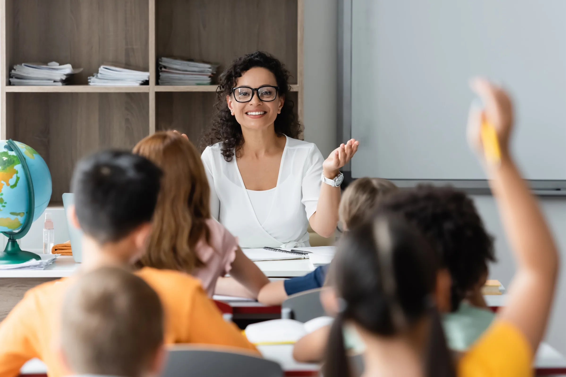 A smiling teacher calls on a student with a raised hand